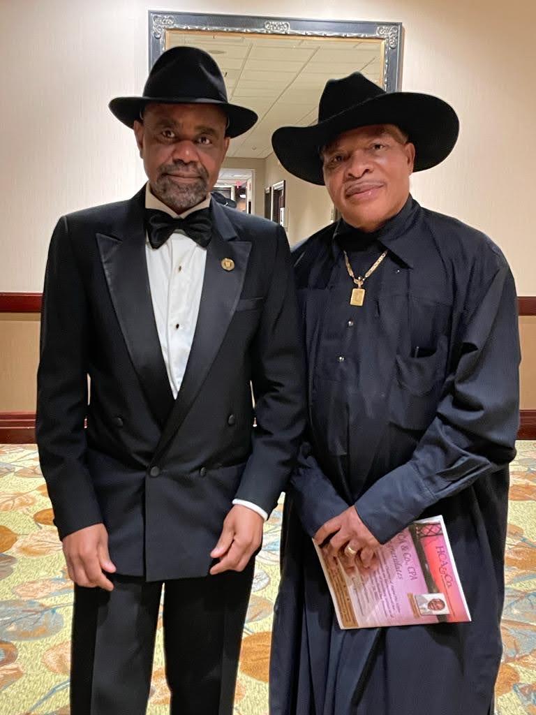 Two community members in formal black attire at an indoor event