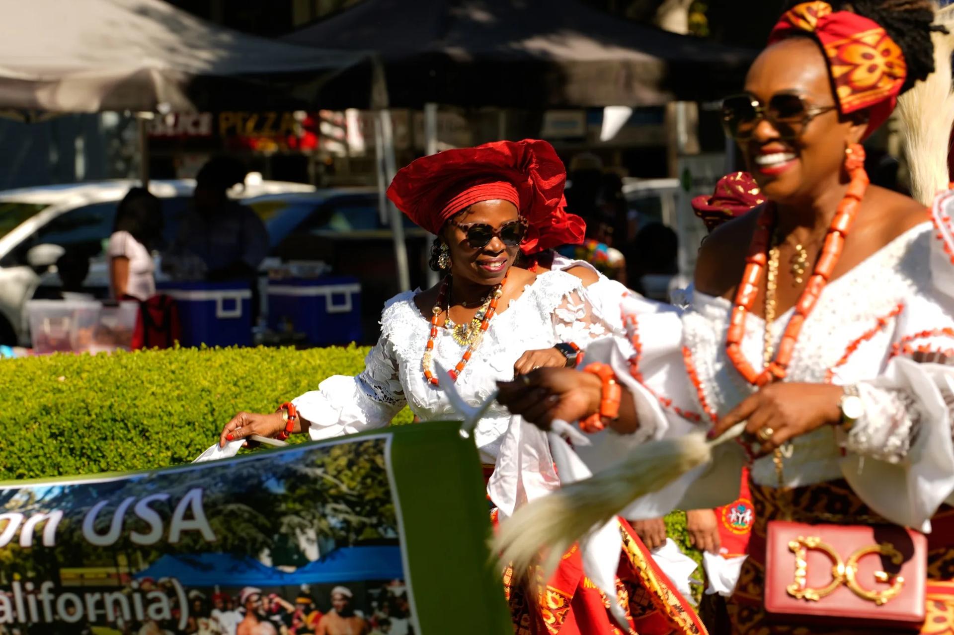 Two women in white lace attire with coral beads celebrating at the festival
